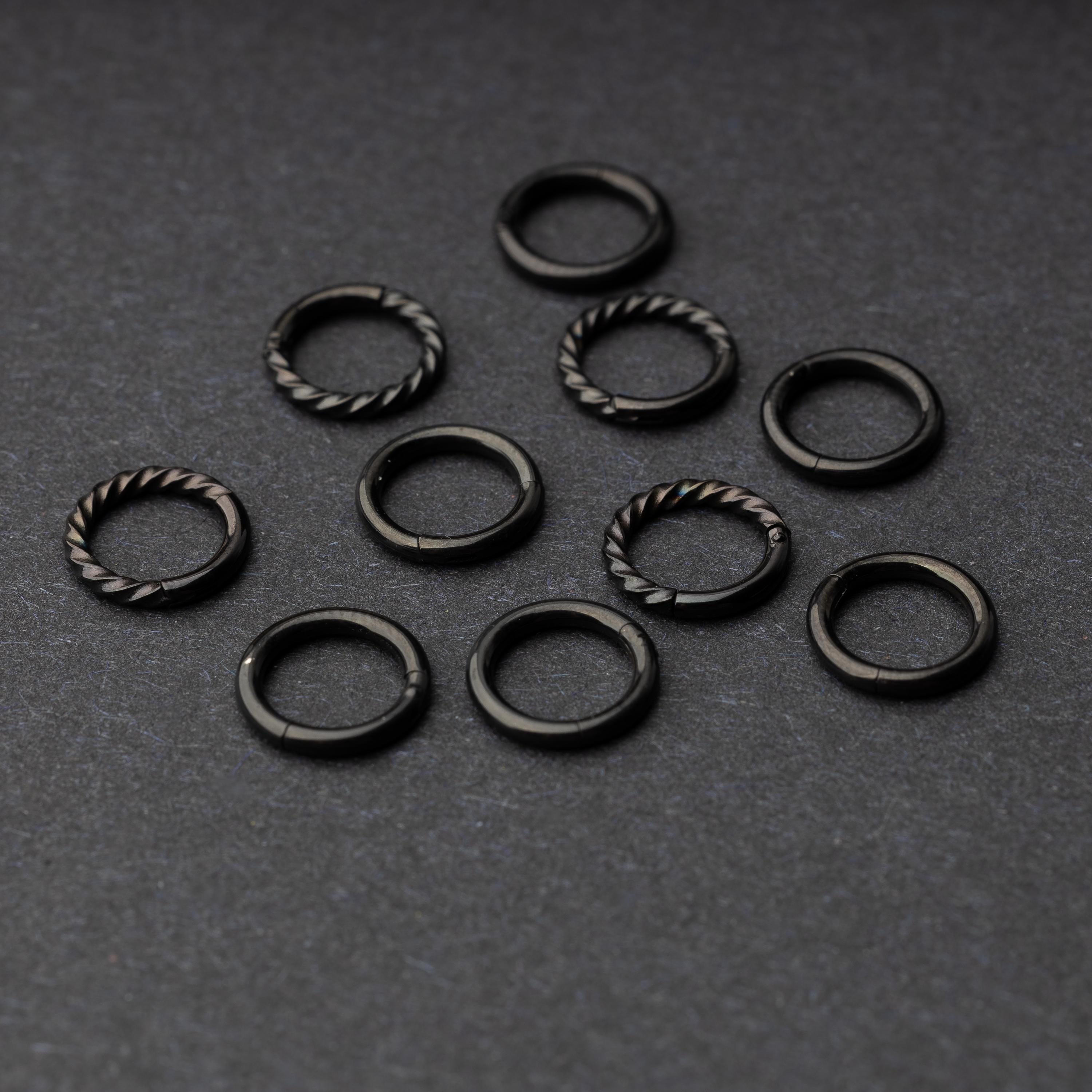 Set of black clicker rings with smooth and twisted designs, displayed on a dark background.