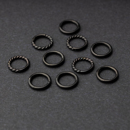 Set of black clicker rings with smooth and twisted designs, displayed on a dark background.