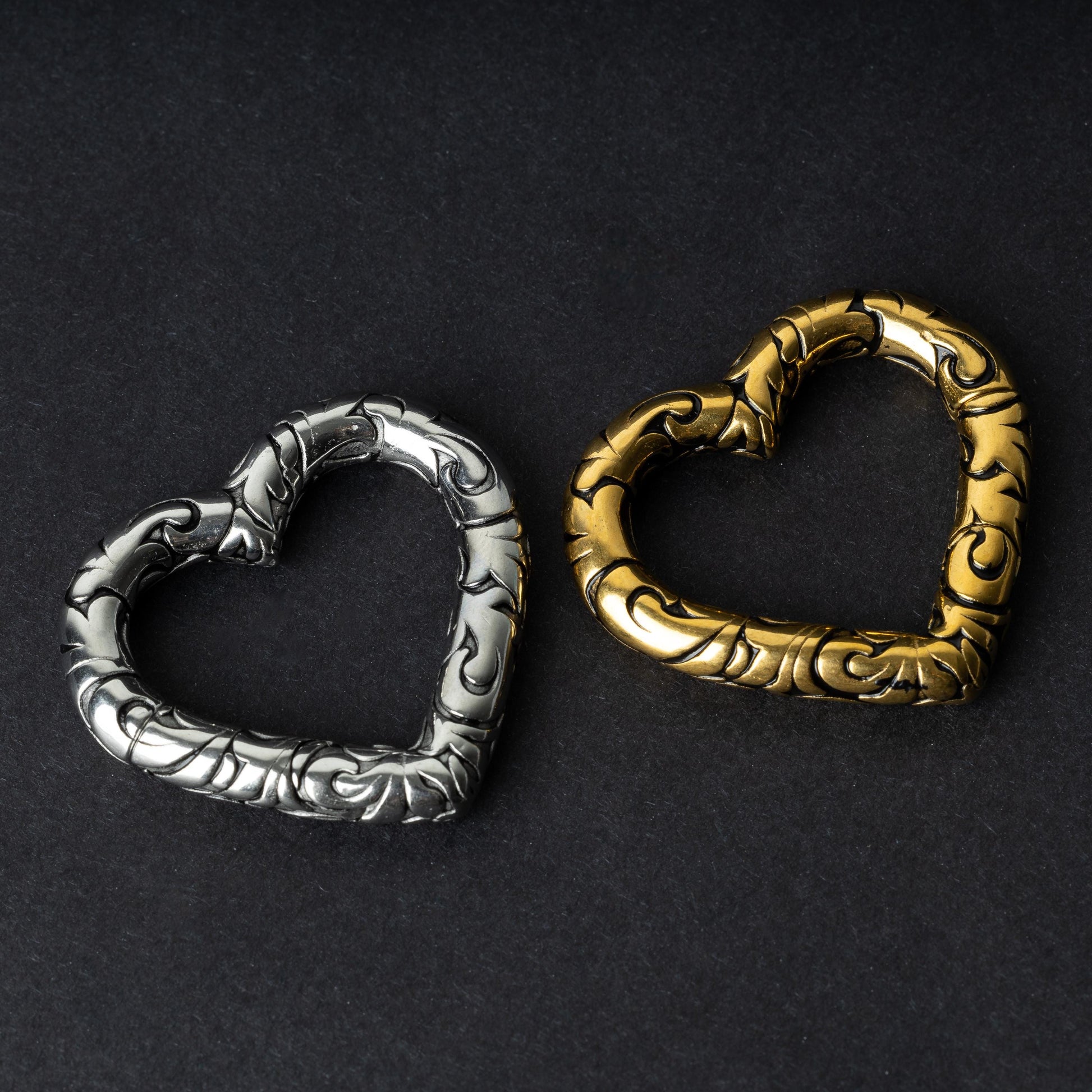 Two heart-shaped engraved saddle plugs in gold and silver tones on a dark background.

