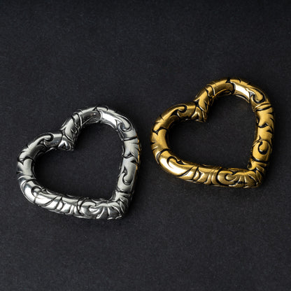 Two heart-shaped engraved saddle plugs in gold and silver tones on a dark background.
