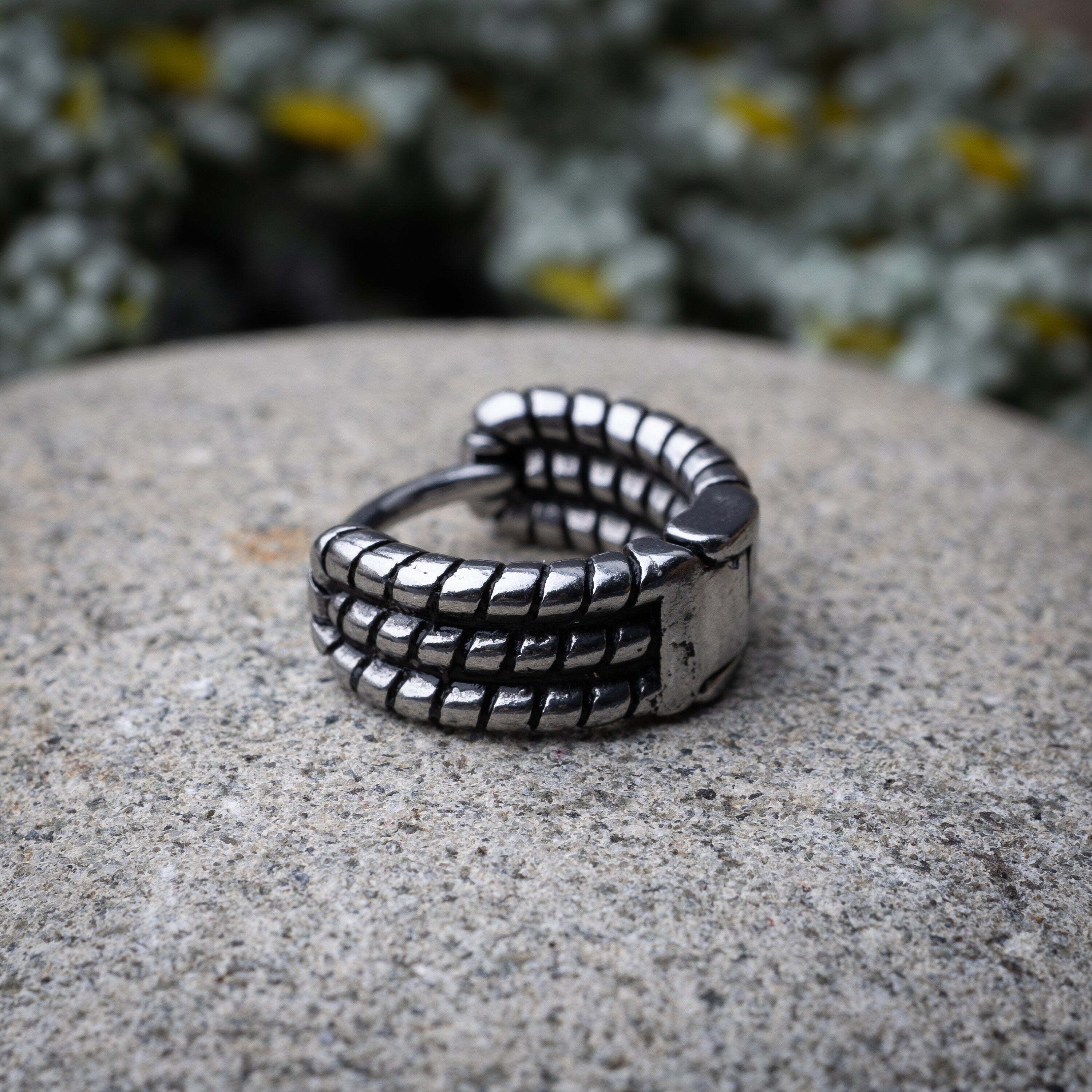 Silver metal hoop earring with a bold, textured grid design, displayed on a stone background.