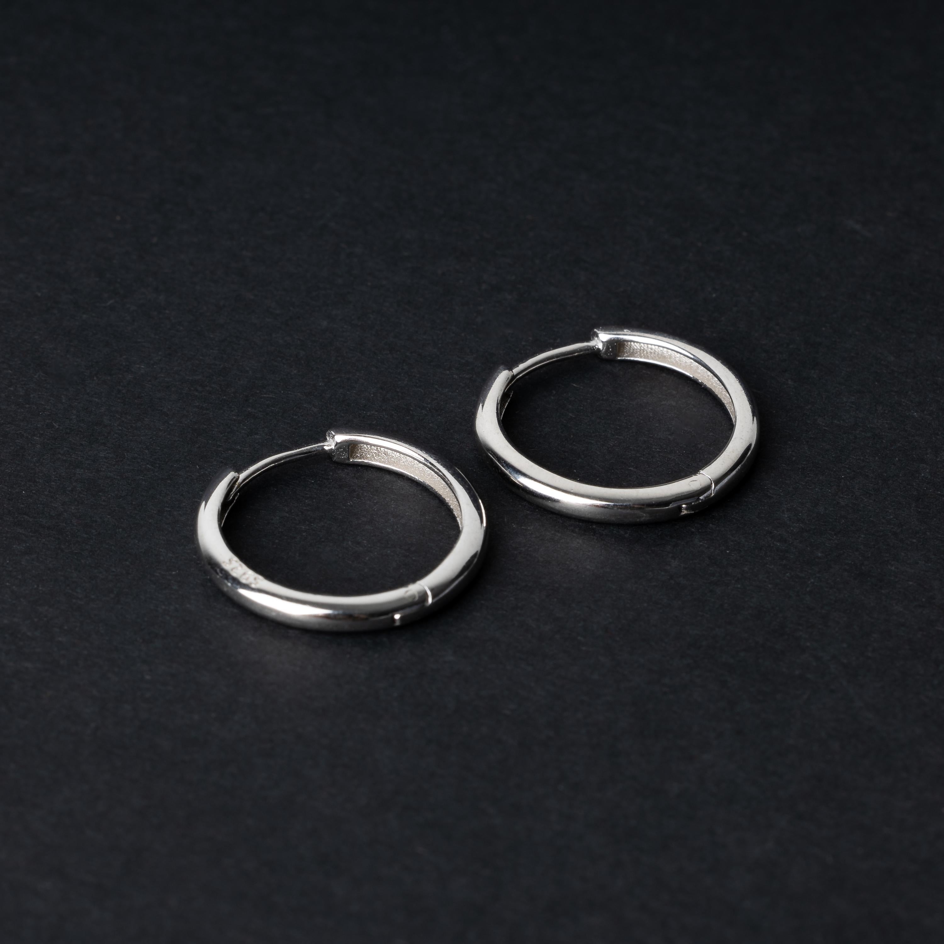A pair of hoop earrings in silver displayed on a dark background