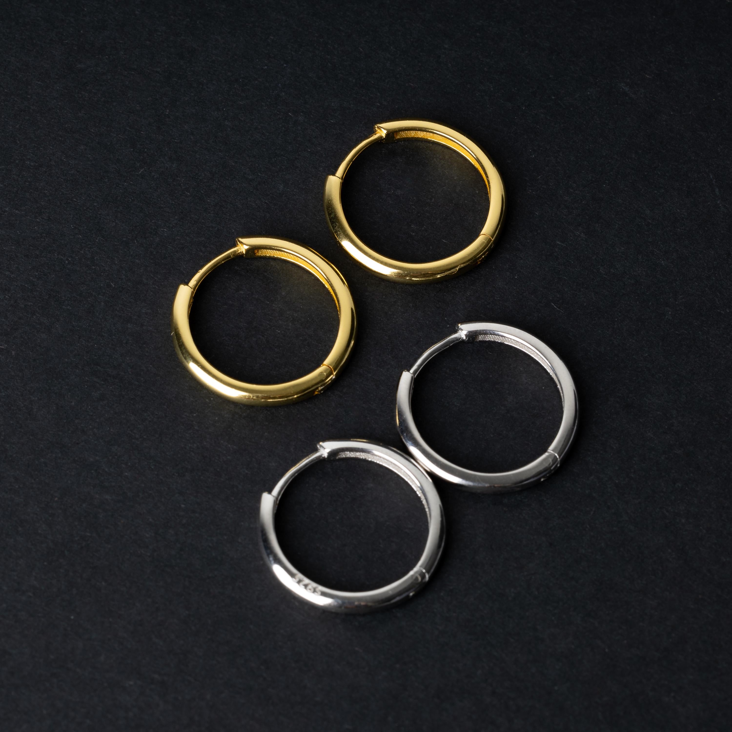 Two pairs of huggie hoop earrings, one in gold and one in silver, displayed on a black background.