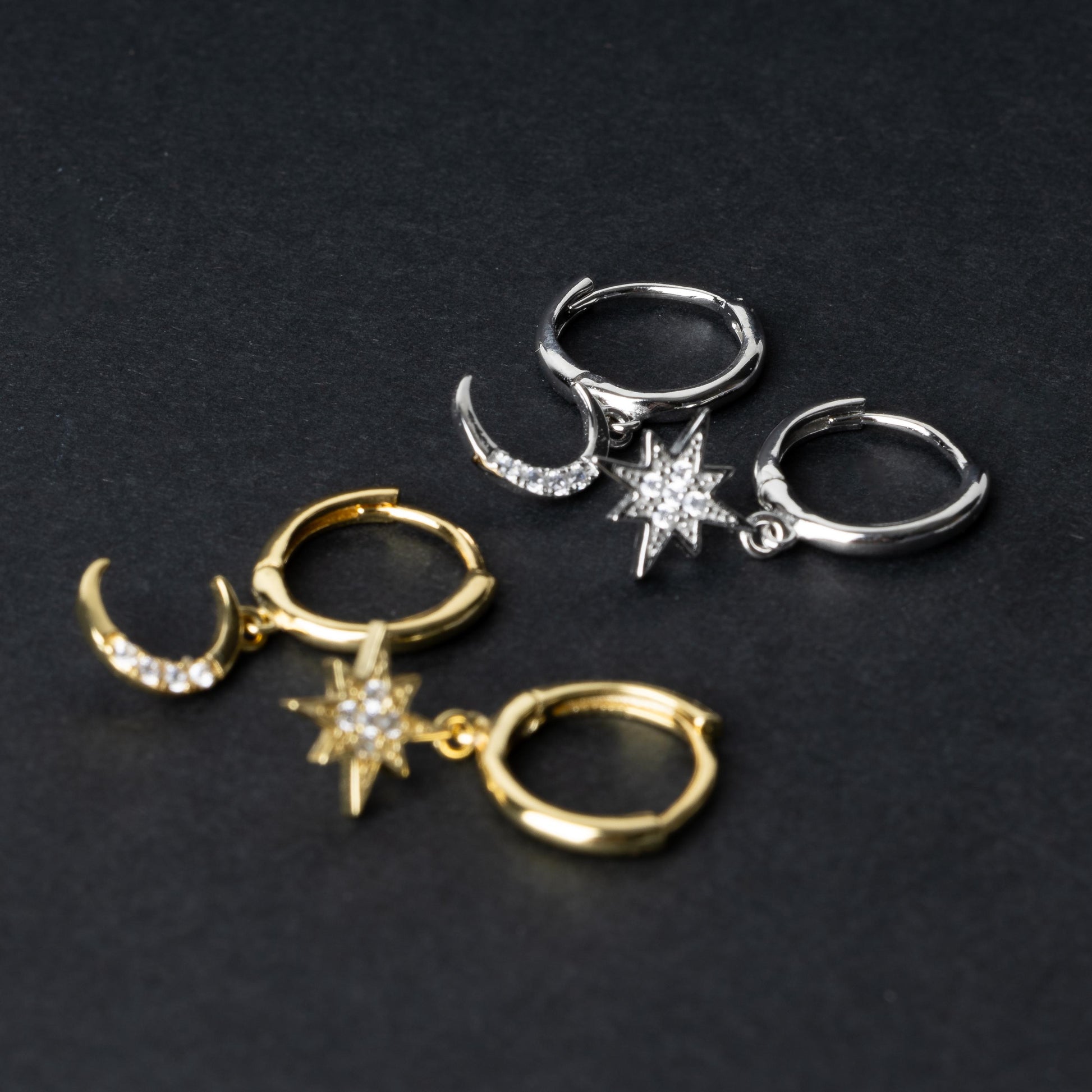 Gold and silver moon and star hoop earrings with cubic zirconia accents, displayed on a dark background.