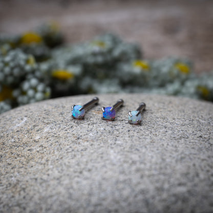 Three opalescent nose studs with prong settings, displayed on a stone background.