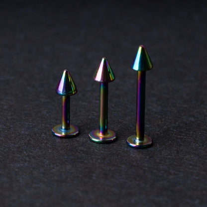 Three rainbow labret studs with cone-shaped tops displayed on a dark background, highlighting their iridescent finish and sleek, durable design.