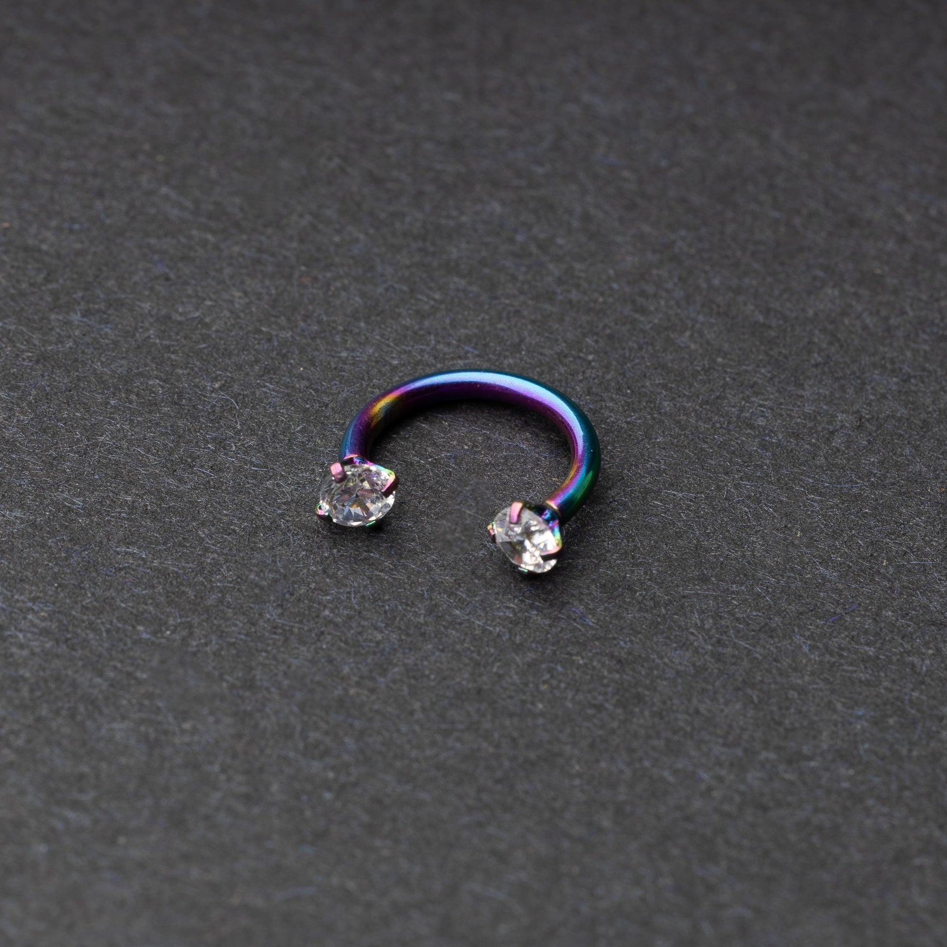 A rainbow jewelled horseshoe hoop with gemstone ends, displayed on a dark background.