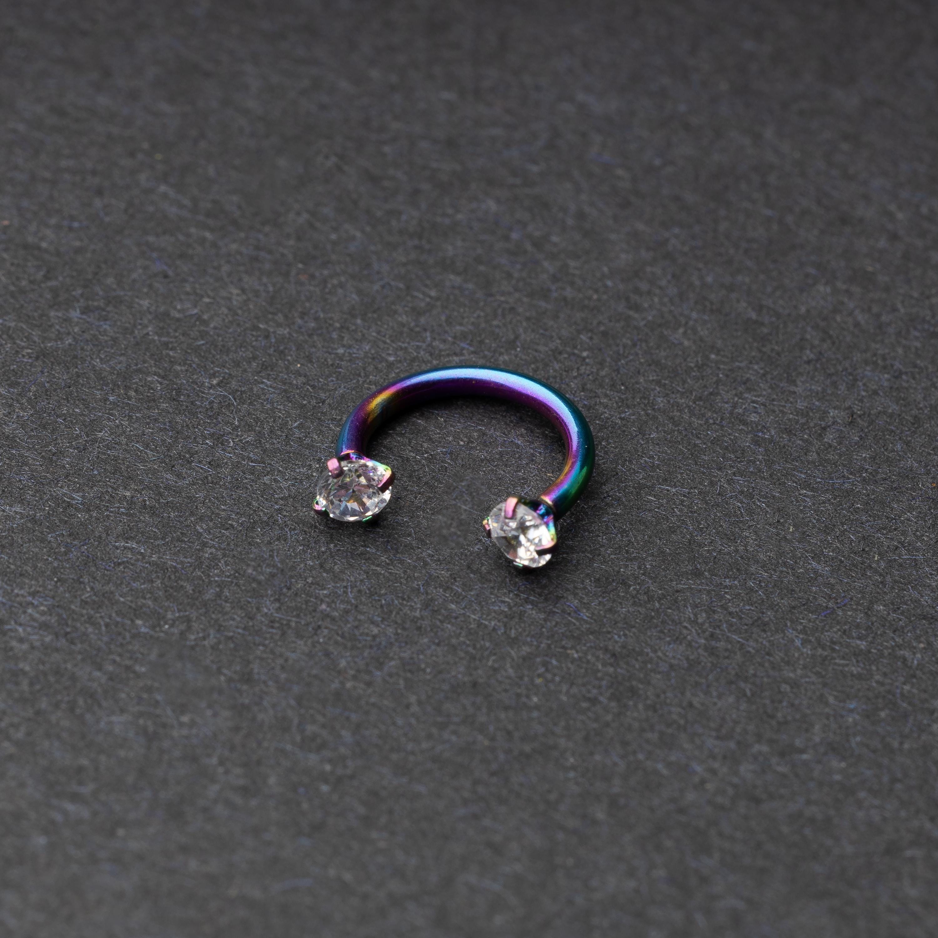A rainbow jewelled horseshoe hoop with gemstone ends, displayed on a dark background.