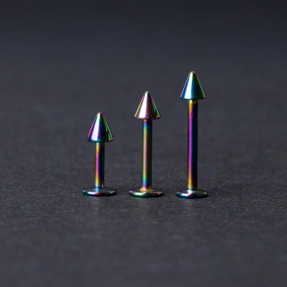 Three rainbow labret studs with cone-shaped tops displayed on a dark background, highlighting their iridescent finish and sleek, durable design.