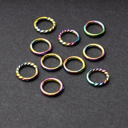 Set of rainbow clicker rings with smooth and twisted designs, displayed on a dark background.