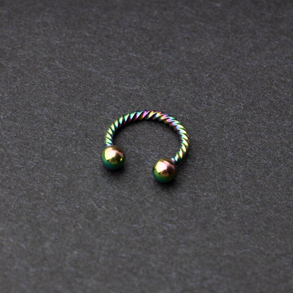Twisted horseshoe barbells in rainbow finish displayed on a dark background, highlighting their bold and unique design.