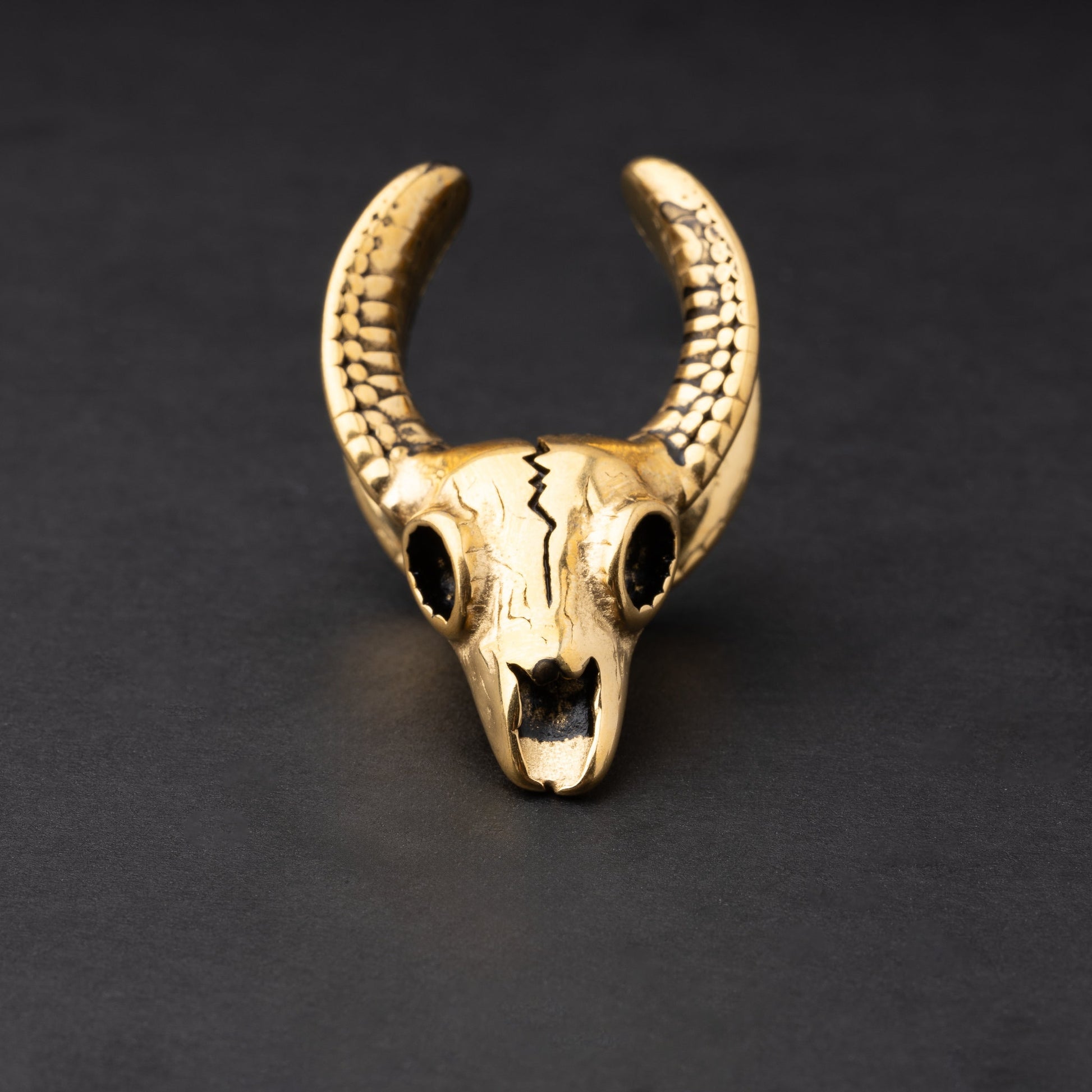 Ram skull saddle tunnels in gold showcasing intricate skull details and bold design on a dark background.