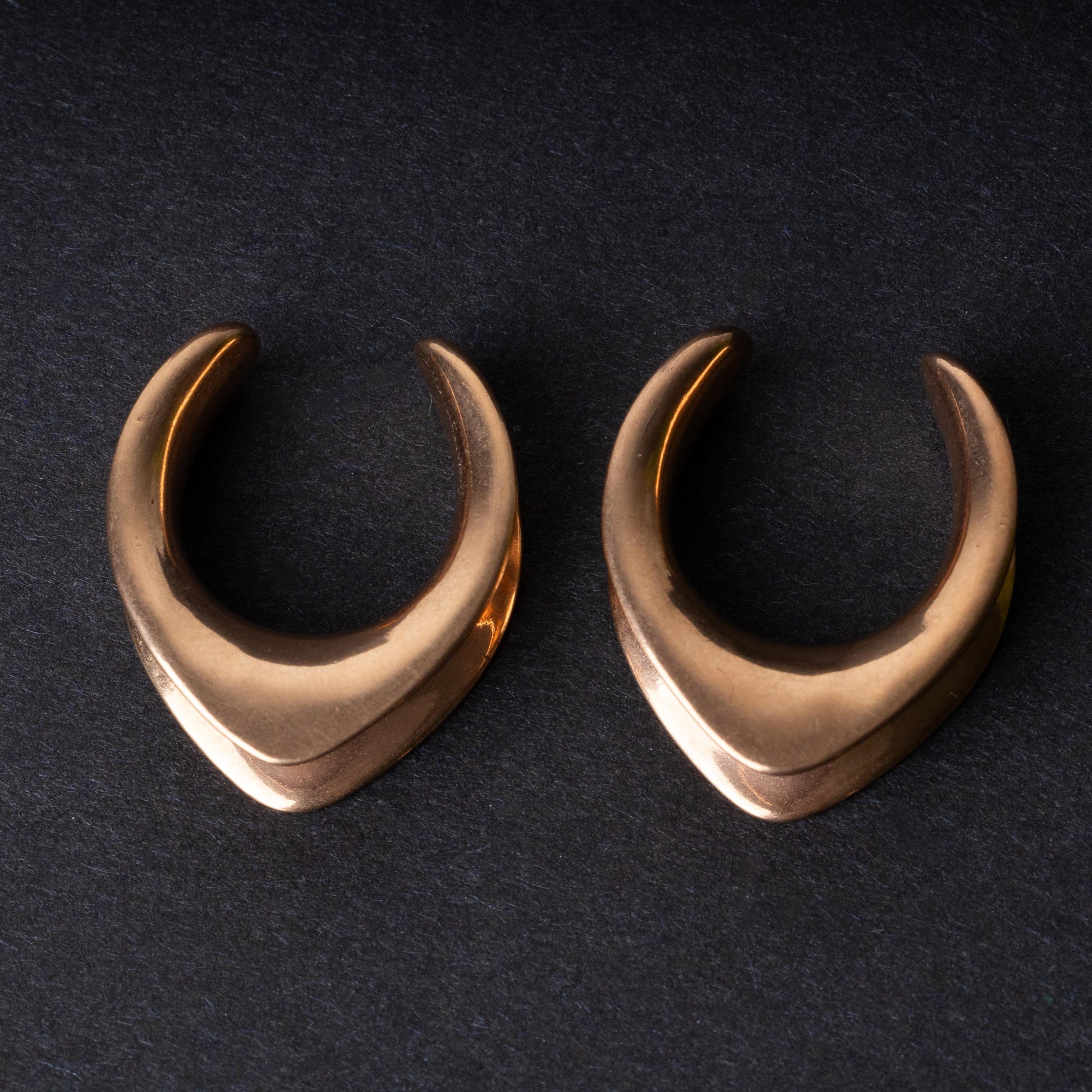 Double-flared metal tunnels for stretched ears in a rose gold finish, displayed on a dark background.
