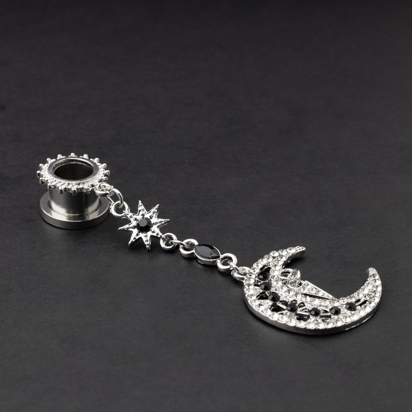A pair of silver ear hangers for stretched ears with dangling crescent moon and star designs, adorned with black and clear rhinestones, displayed on a dark background.