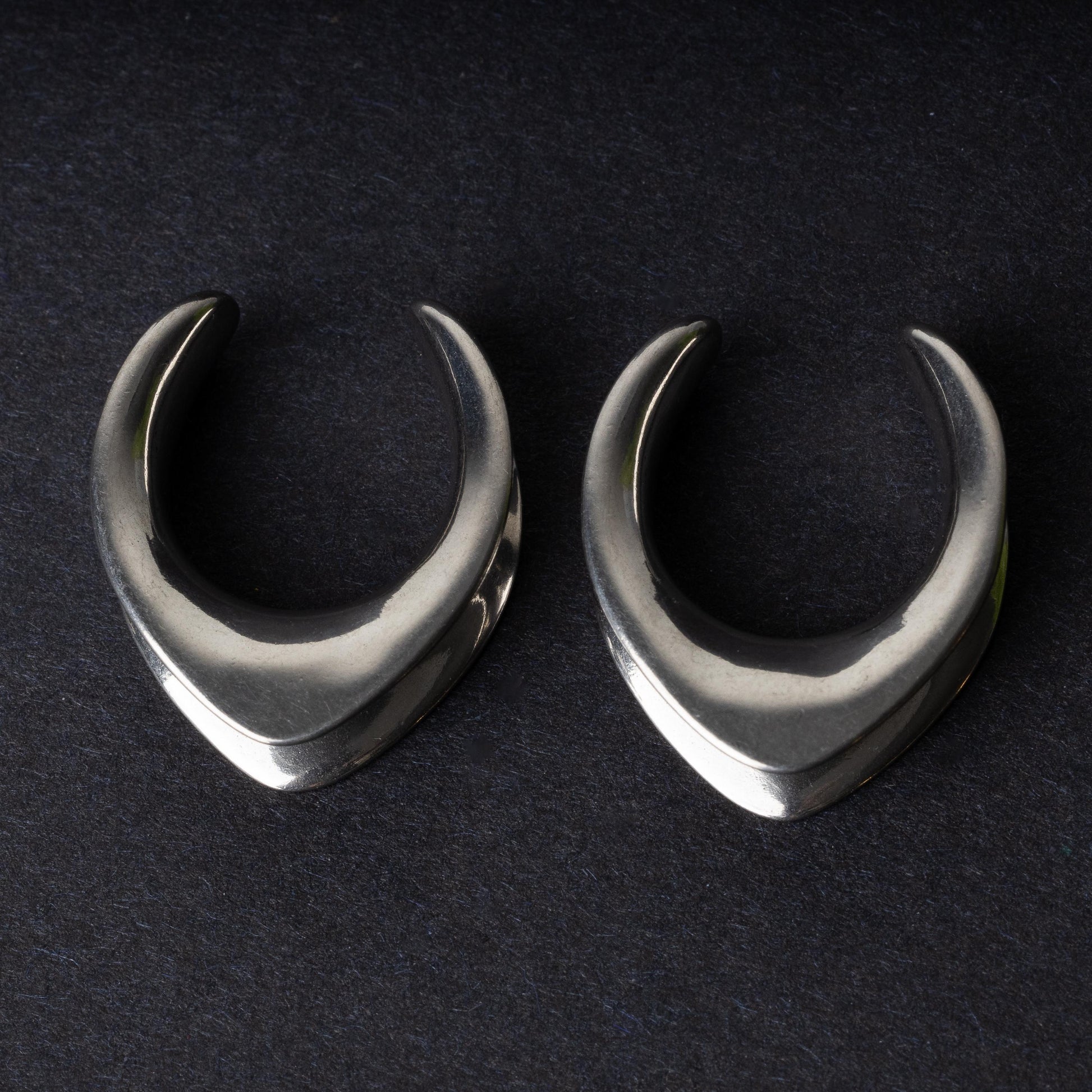 Double-flared metal tunnels for stretched ears in a silver finish, displayed on a dark background.
