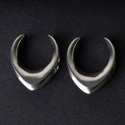 Double-flared metal tunnels for stretched ears in a silver finish, displayed on a dark background.
