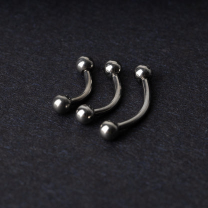 Three silver stainless steel curved barbells with polished ball ends, displayed on a dark textured background.