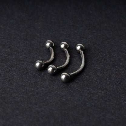 Three silver stainless steel curved barbells with polished ball ends, displayed on a dark textured background.
