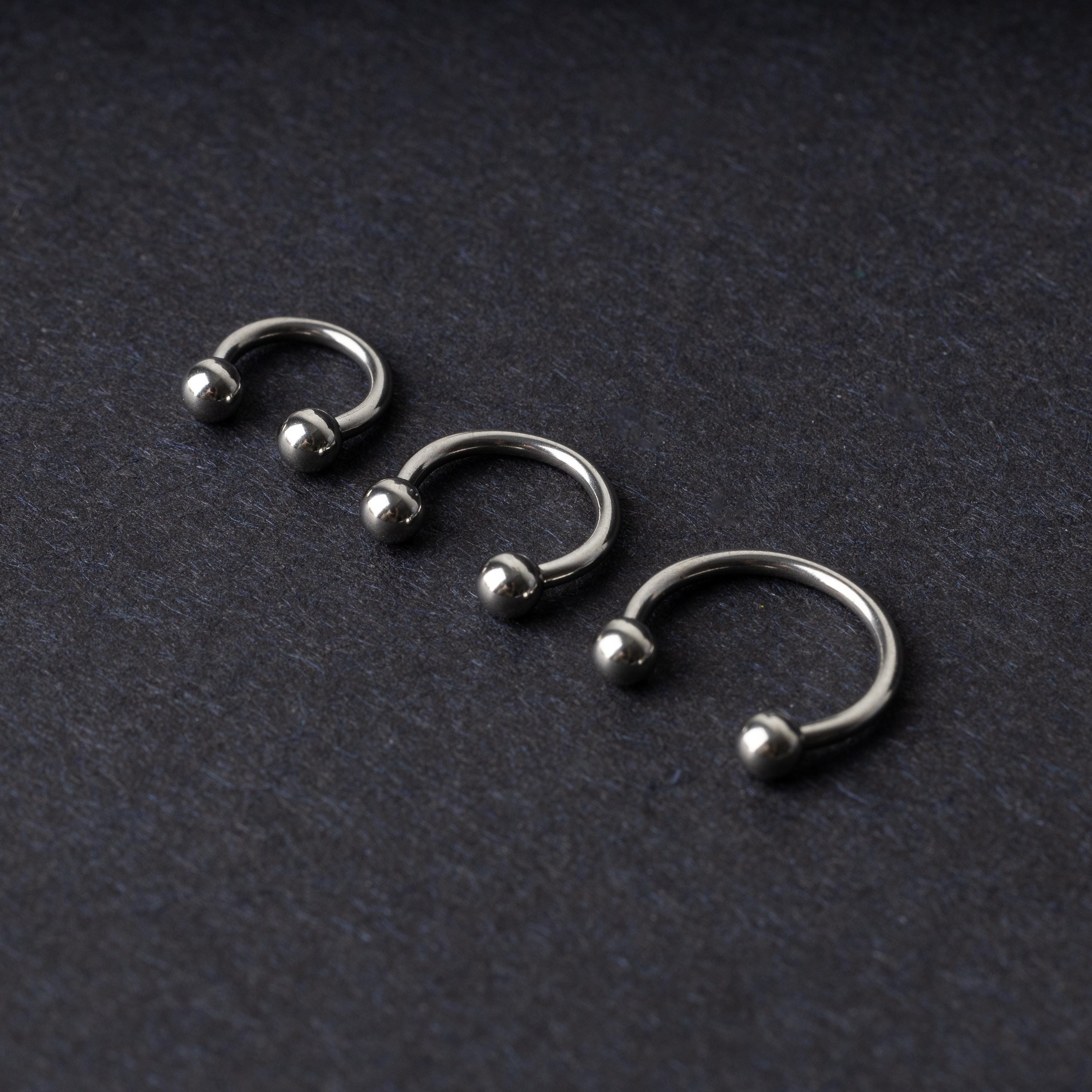 Three silver stainless steel horseshoe hoops with polished ball ends, displayed on a dark textured background.