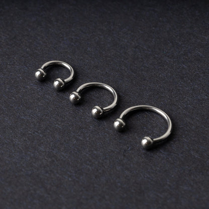 Three silver stainless steel horseshoe hoops with polished ball ends, displayed on a dark textured background.