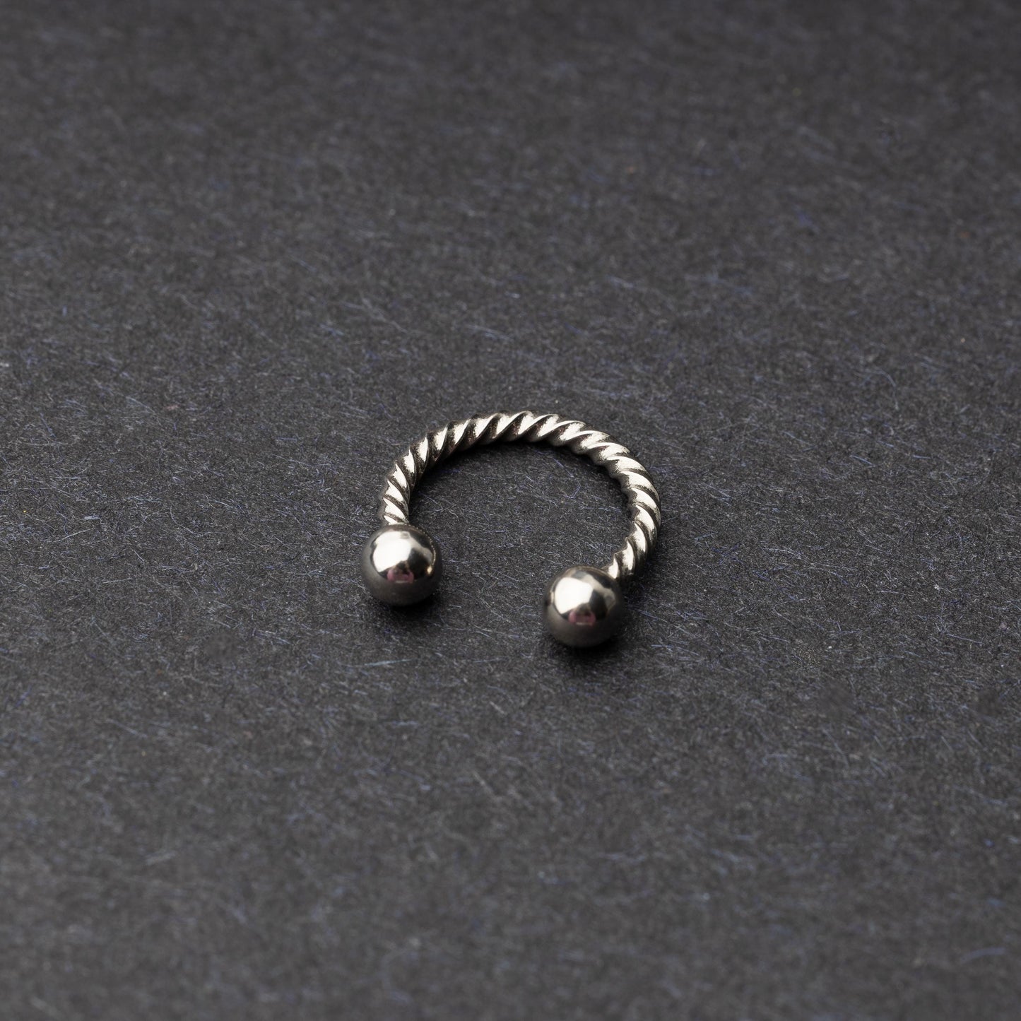 Twisted horseshoe barbells in silver finish displayed on a dark background, highlighting their bold and unique design.