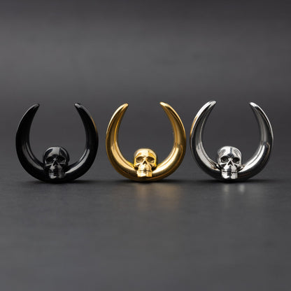 Three skull saddle tunnels in black, gold, and silver finishes displayed on a dark background, showcasing their bold and detailed skull design.