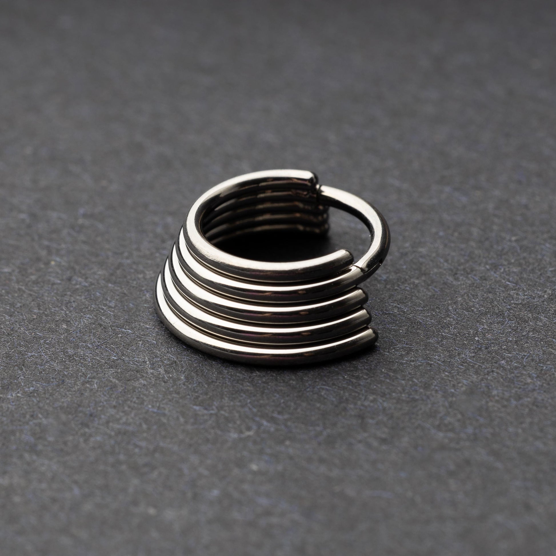 A silver-tone septum clicker with a stacked multi-ring design, displayed on a dark background, showcasing its bold and modern style.
