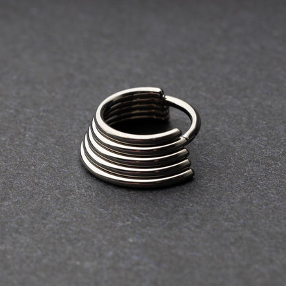 A silver-tone septum clicker with a stacked multi-ring design, displayed on a dark background, showcasing its bold and modern style.
