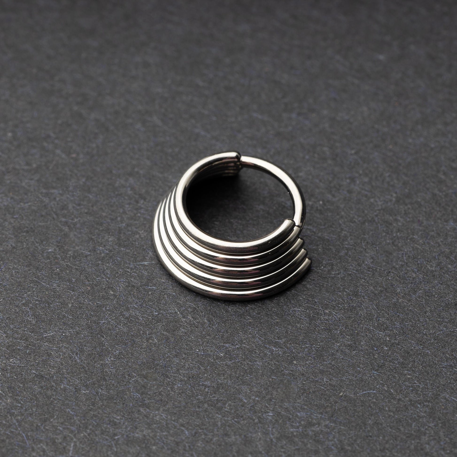 A silver-tone septum clicker with a stacked multi-ring design, displayed on a dark background, showcasing its bold and modern style.

