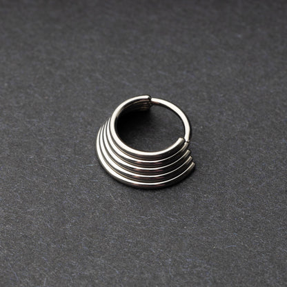 A silver-tone septum clicker with a stacked multi-ring design, displayed on a dark background, showcasing its bold and modern style.

