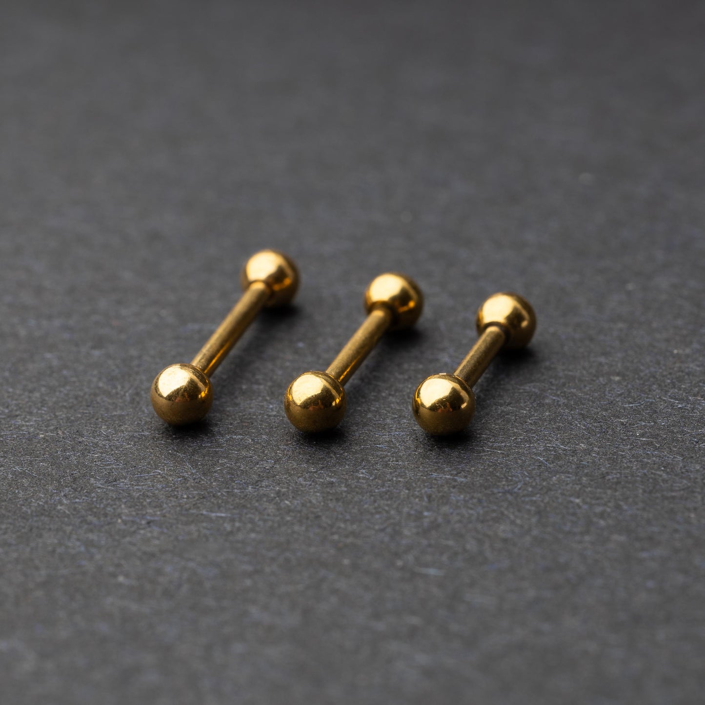 Gold-tone stainless steel barbells with polished spheres on a dark background.