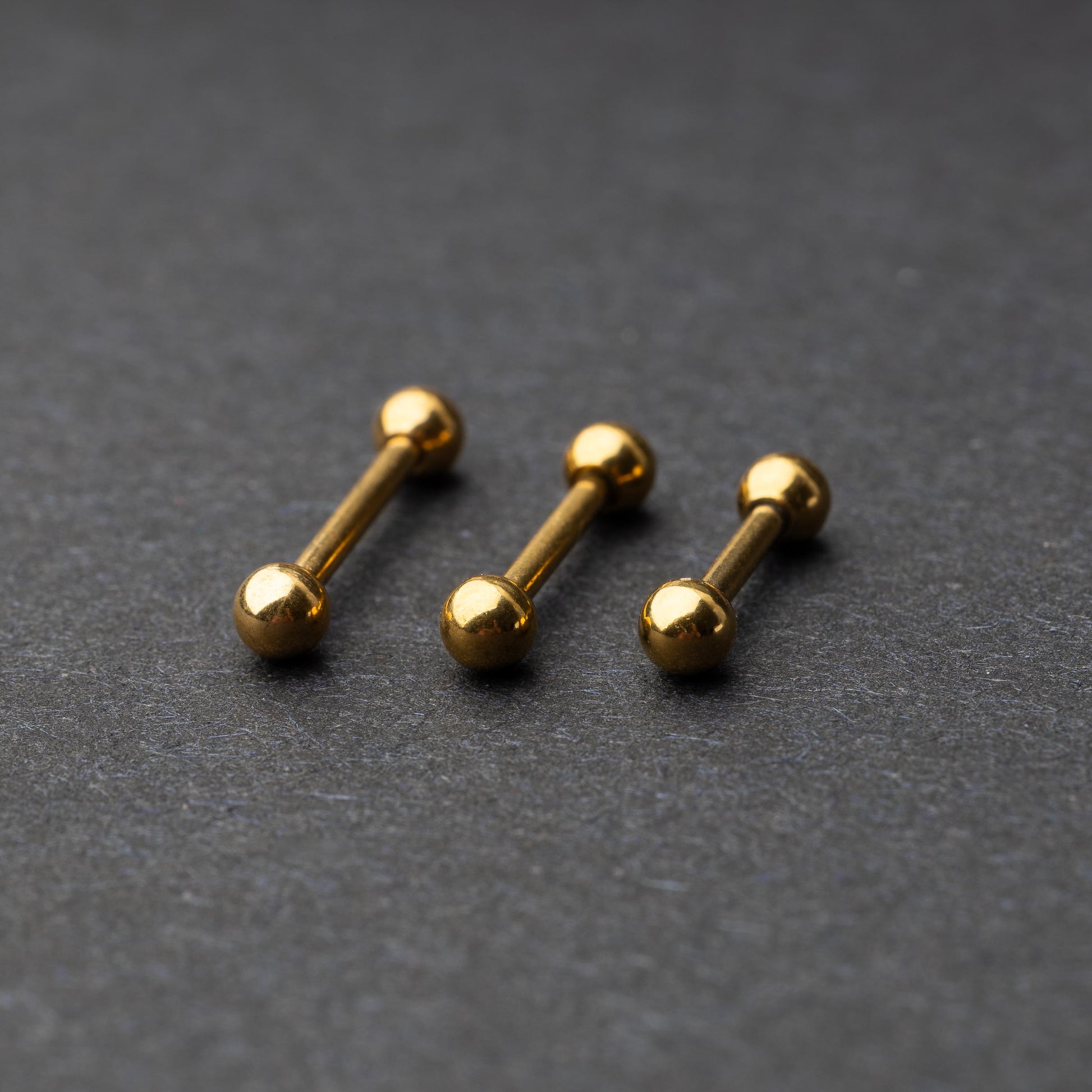 Gold-tone stainless steel barbells with polished spheres on a dark background.