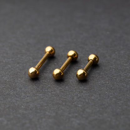 Gold-tone stainless steel barbells with polished spheres on a dark background.