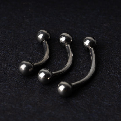 Three silver stainless steel curved barbells with polished ball ends, displayed on a dark textured background.