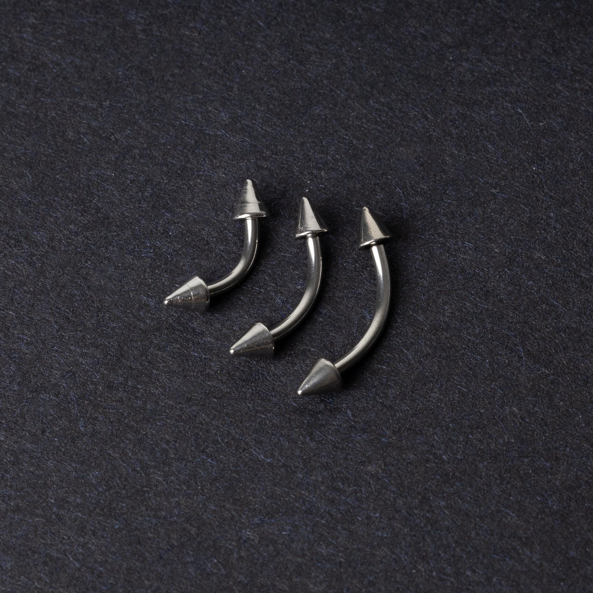 Three stainless steel curved barbells with cone-shaped ends, displayed on a dark background.