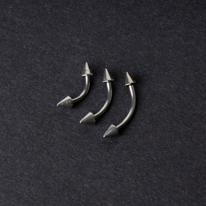 Three stainless steel curved barbells with cone-shaped ends, displayed on a dark background.