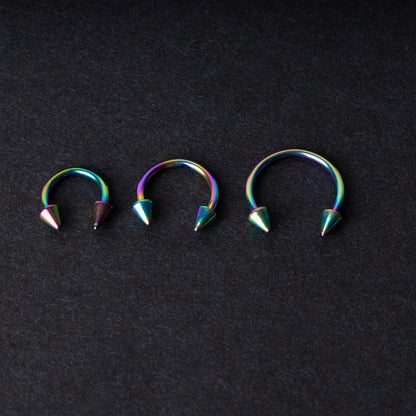 Three stainless steel horseshoe hoops with cone-shaped ends and a rainbow anodized finish displayed on a dark background, showcasing their bold design and vibrant colors.