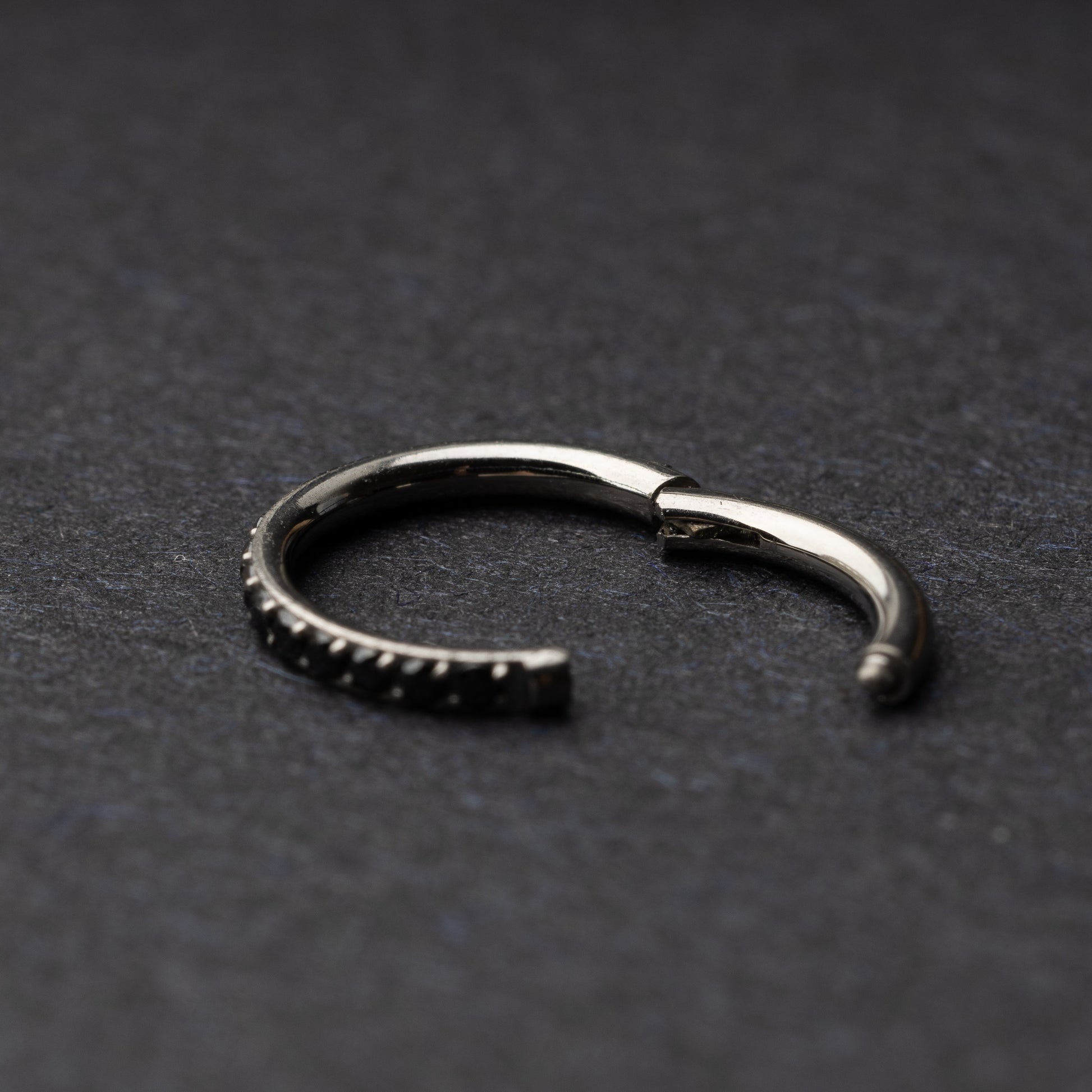 A textured stainless steel seamless ring with a polished finish, placed on a dark, textured background.