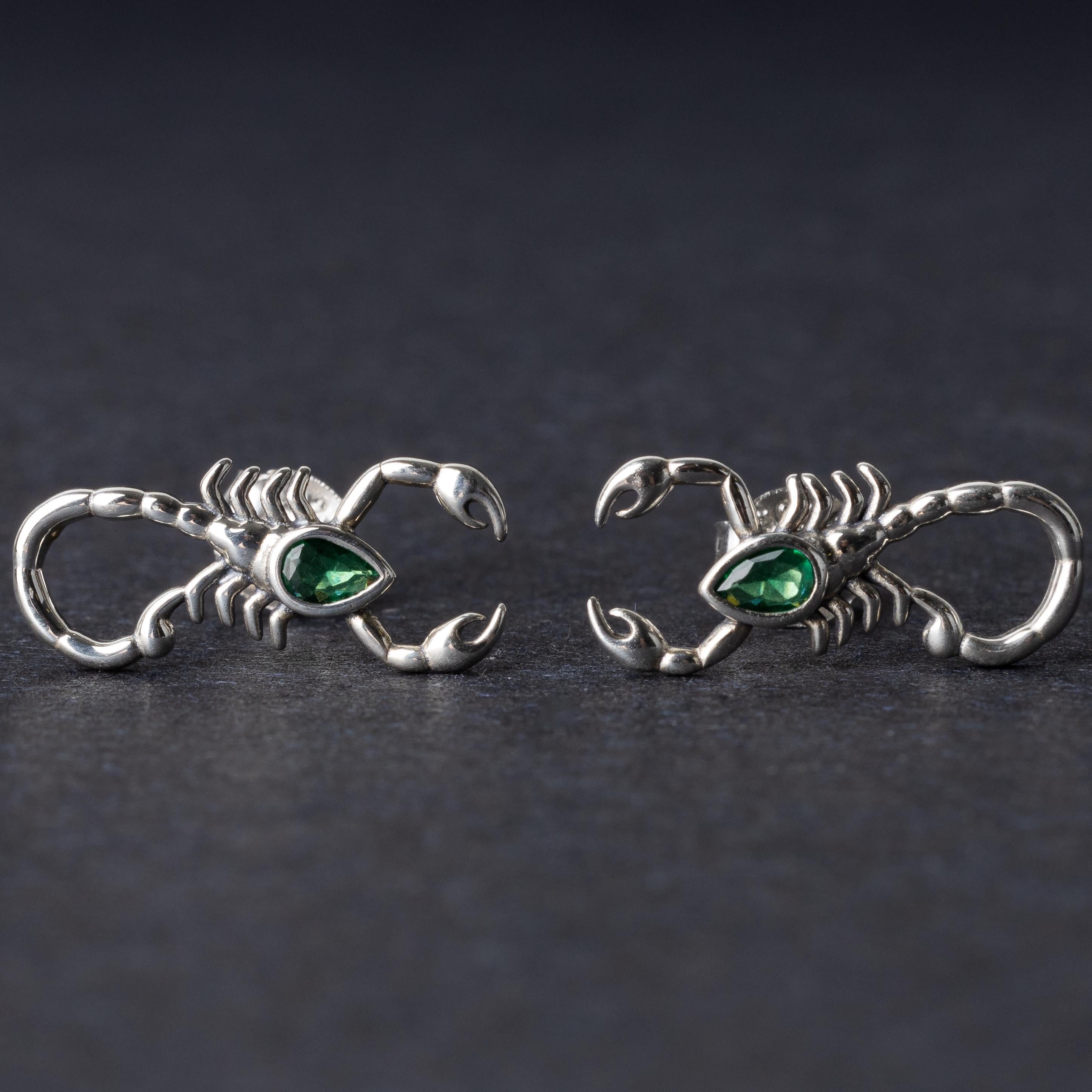 A pair of 925 sterling silver scorpion-shaped earrings with green gemstone accents as eyes, displayed on a dark background.