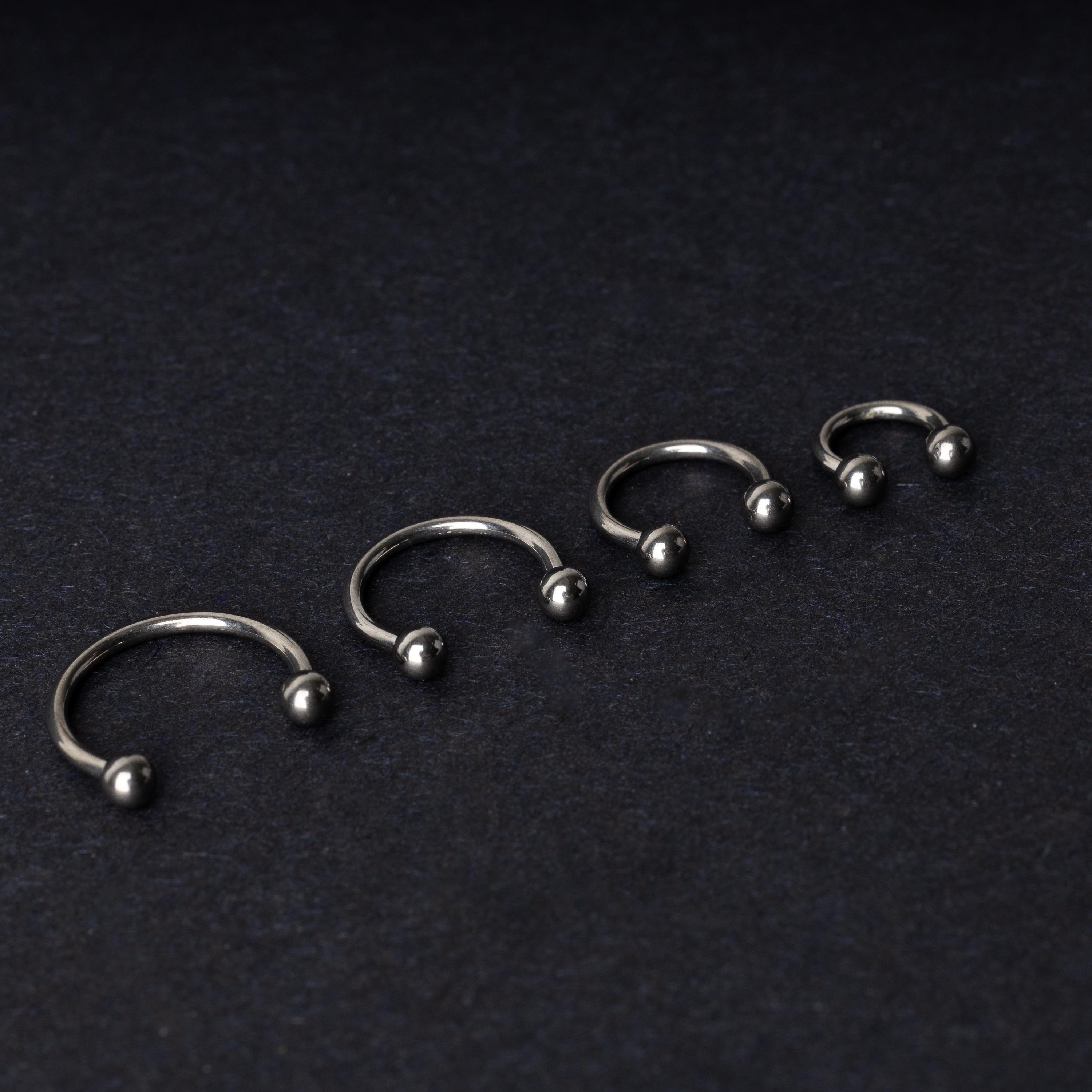 Four titanium horseshoe hoops with ball ends, arranged from largest to smallest on a dark background.