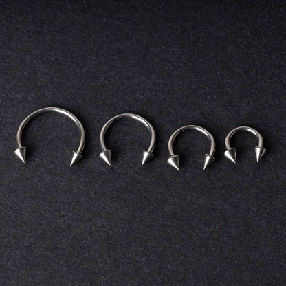 Four titanium horseshoe hoops with pointed cone ends, lined up on a dark background.