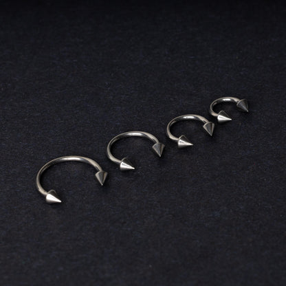 Four titanium horseshoe hoops with pointed cone ends, lined up on a dark background.