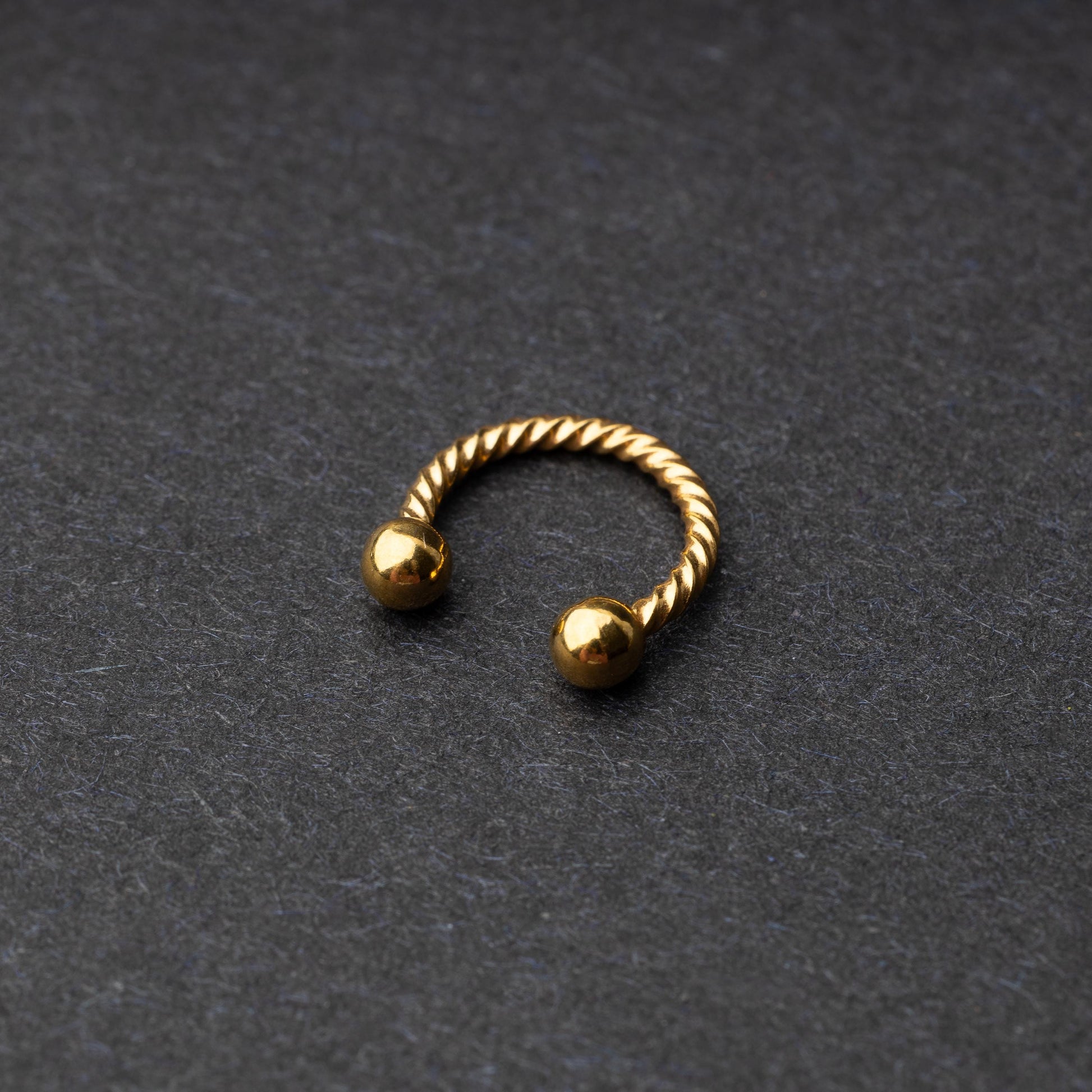 Twisted horseshoe barbells in gold finish displayed on a dark background, highlighting their bold and unique design.