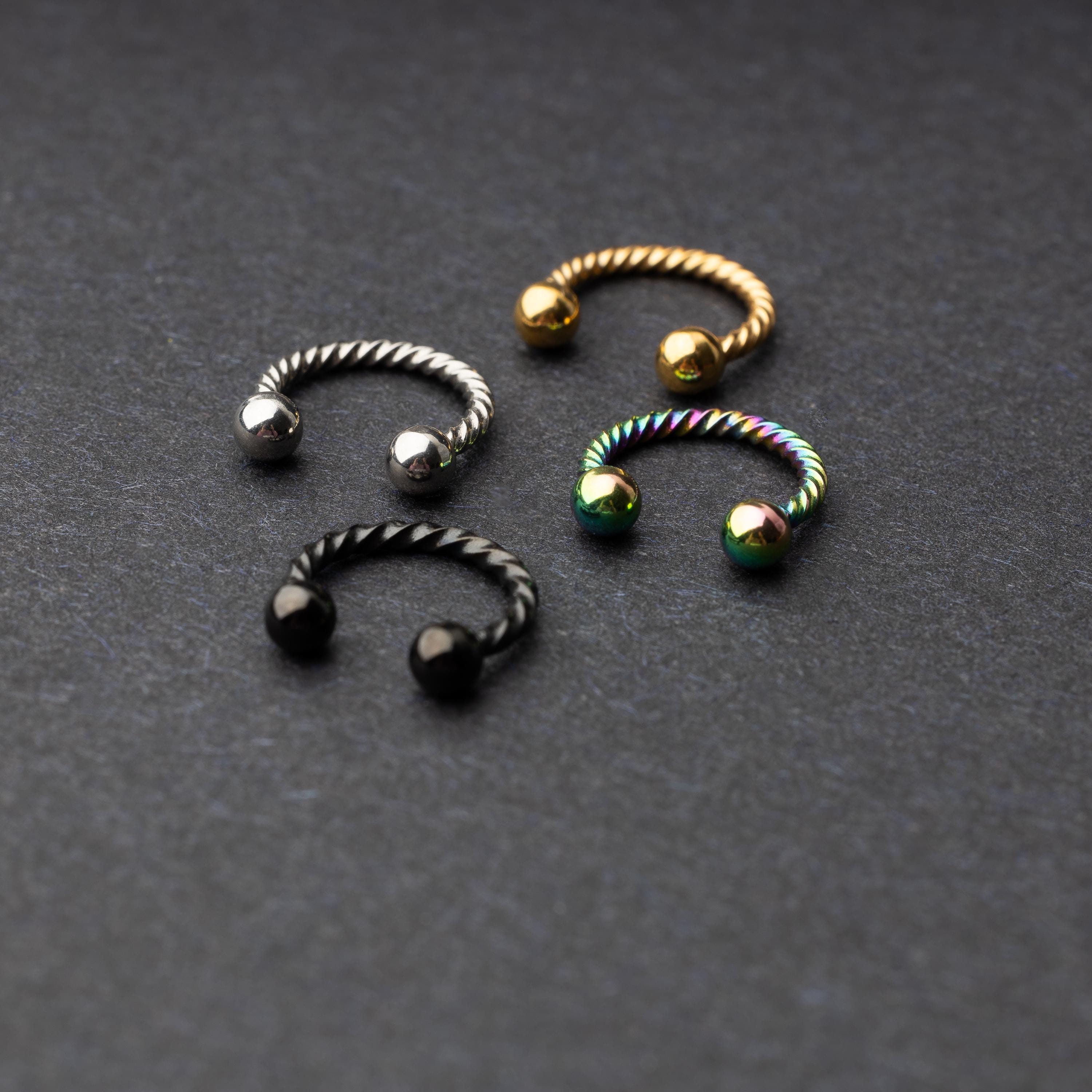 Twisted horseshoe barbells in silver, rainbow, gold, and black finishes displayed on a dark background, highlighting their bold and unique design.