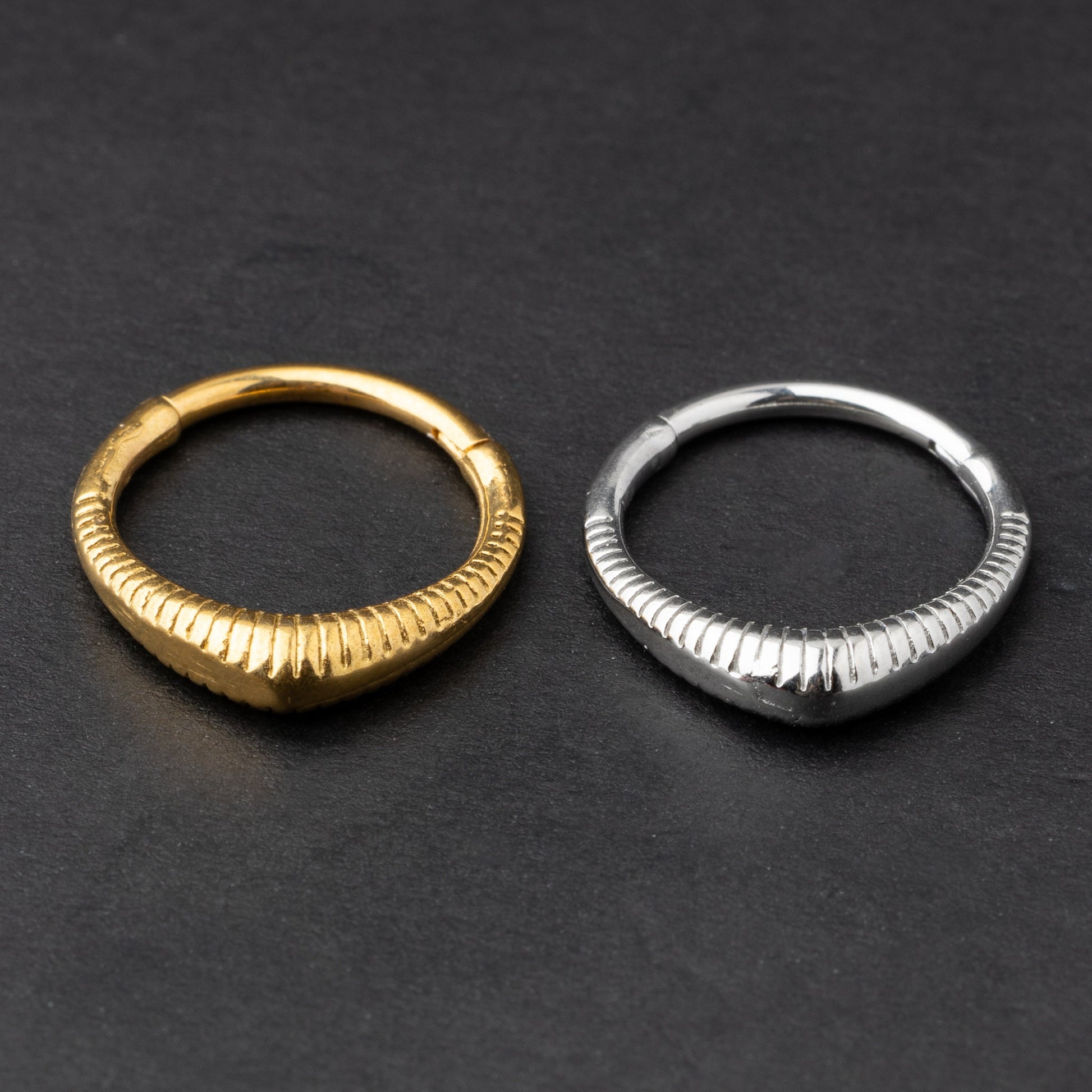 Gold and silver ribbed septum clicker jewelry displayed on a dark background, showcasing a sleek, modern design